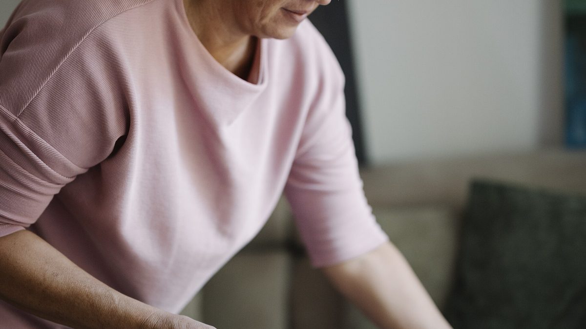 Middle-aged woman cleaning a couch with a handheld vacuum in a living room during the day.jpg